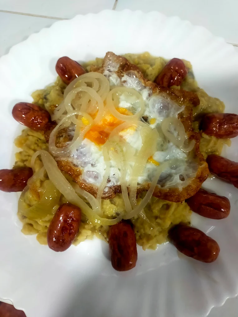 Mangú dominicano con salchicha y coronado por un huevo fritos y cebolla frita.